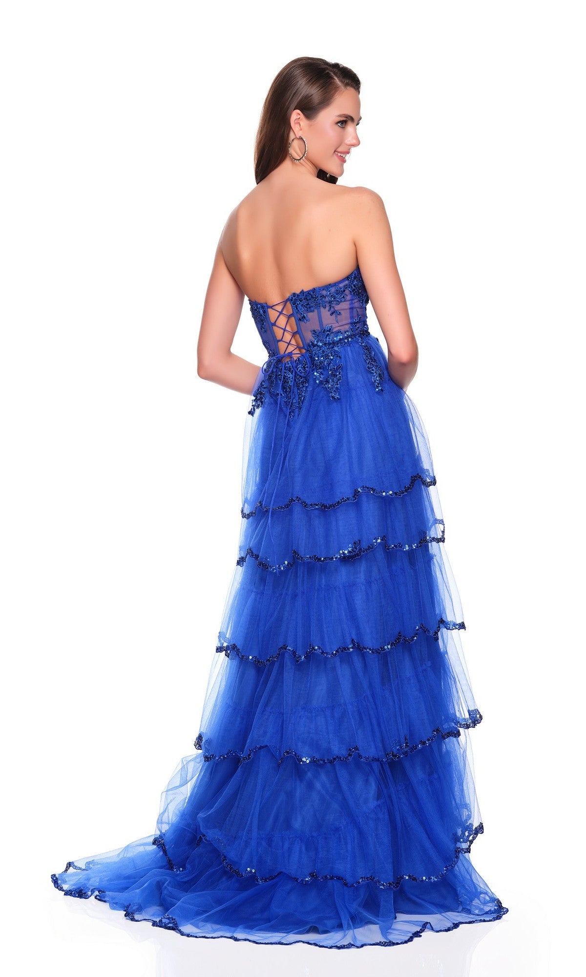 A woman in the Dave and Johnny 12871 long prom dress, featuring a strapless blue bodice, tiered tulle A-line skirt, and lace-up back, stands facing away from the camera.